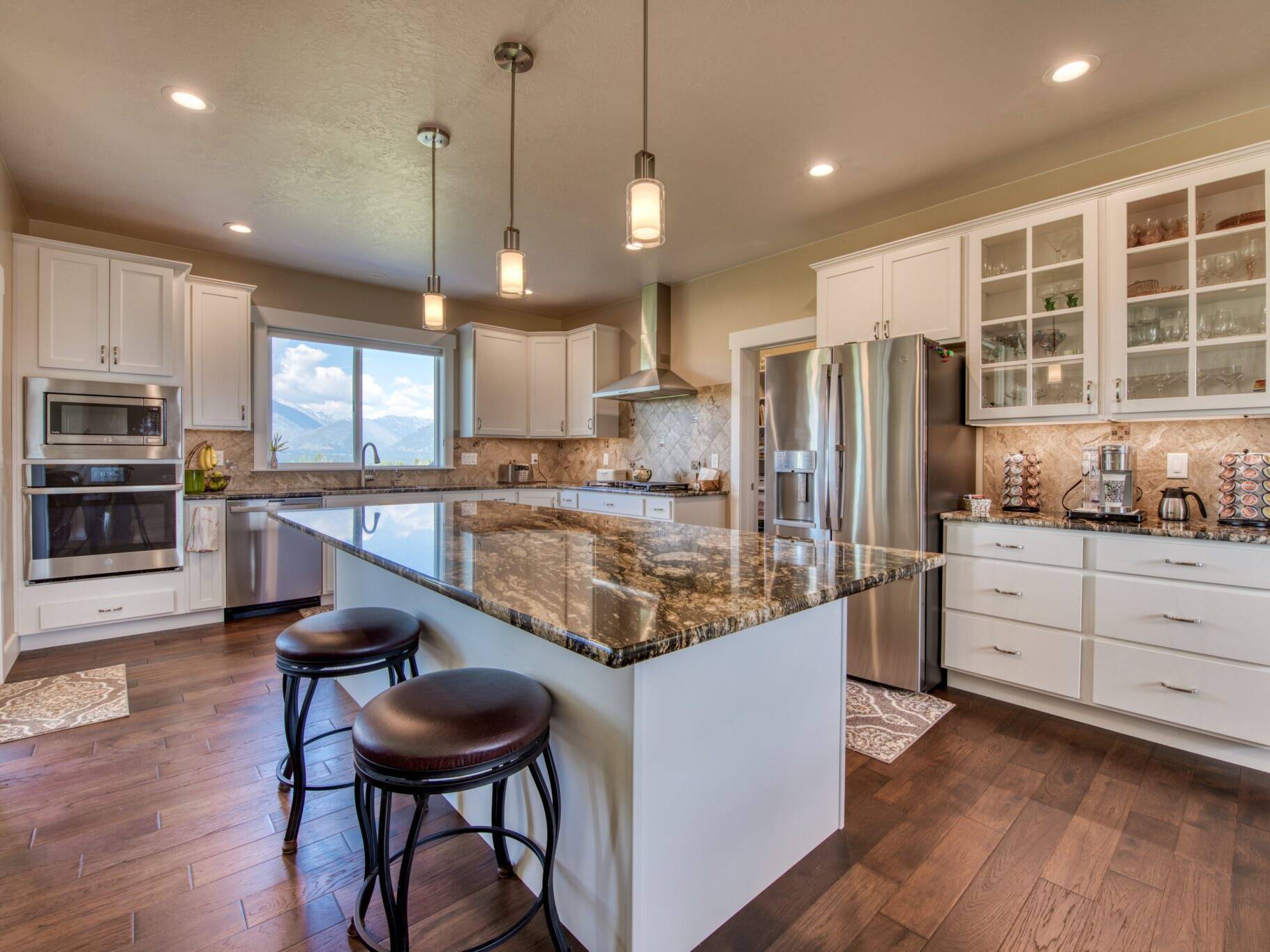 Kitchen with island, granite countertops, tile backsplash, and wood flooring in a custom home built by Big Sky Builders of Montana in Hamilton, MT