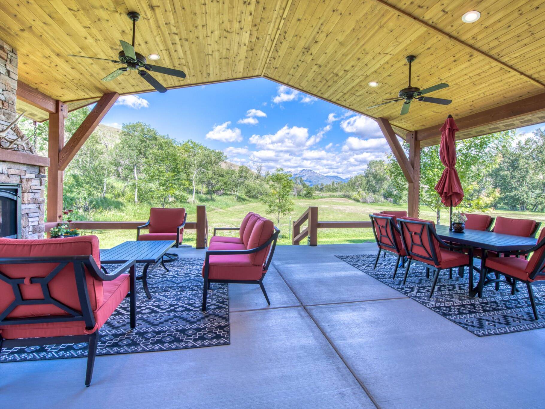 Covered back patio with vaulted wood ceilings, accent beams, a gas fireplace with raised hearth, stone masonry and a mantle in a custom home near Hamilton, MT