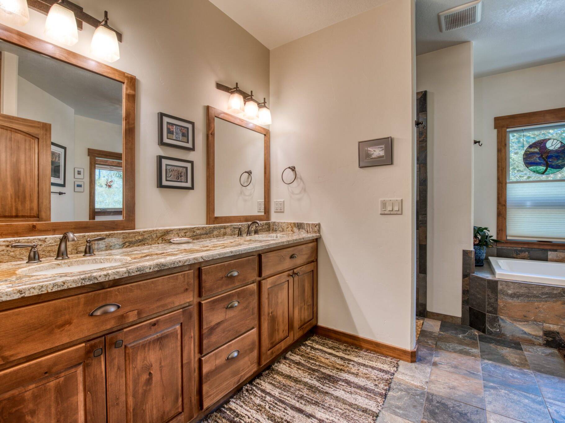 Master bathroom with tile floors, granite countertops, and a soaking tub set in a tiled tub deck with a large window in a custom home near Hamilton, MT