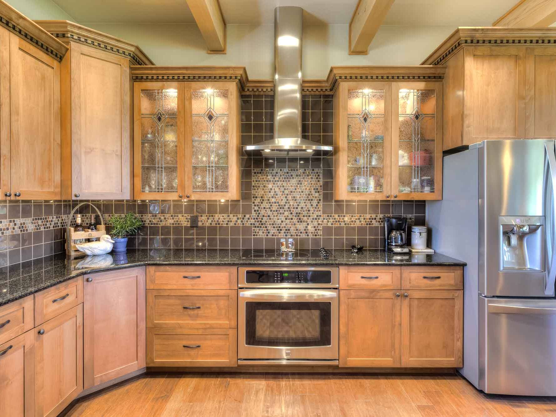 Kitchen with granite countertops, tile backsplash, and custom glass in the cabinet doors in a custom home built by Big Sky Builders in Hamilton Montana