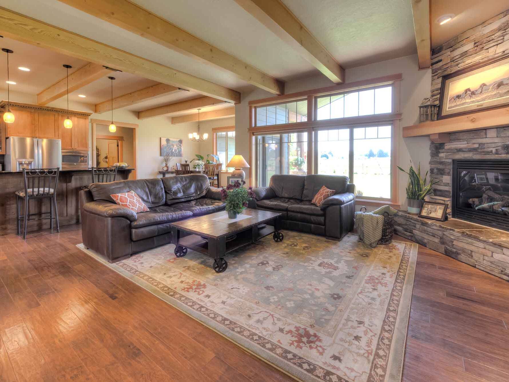 Living room with ceiling beams, a corner fireplace, and wood flooring inside a custom home built by Big Sky Builders in Hamilton Montana
