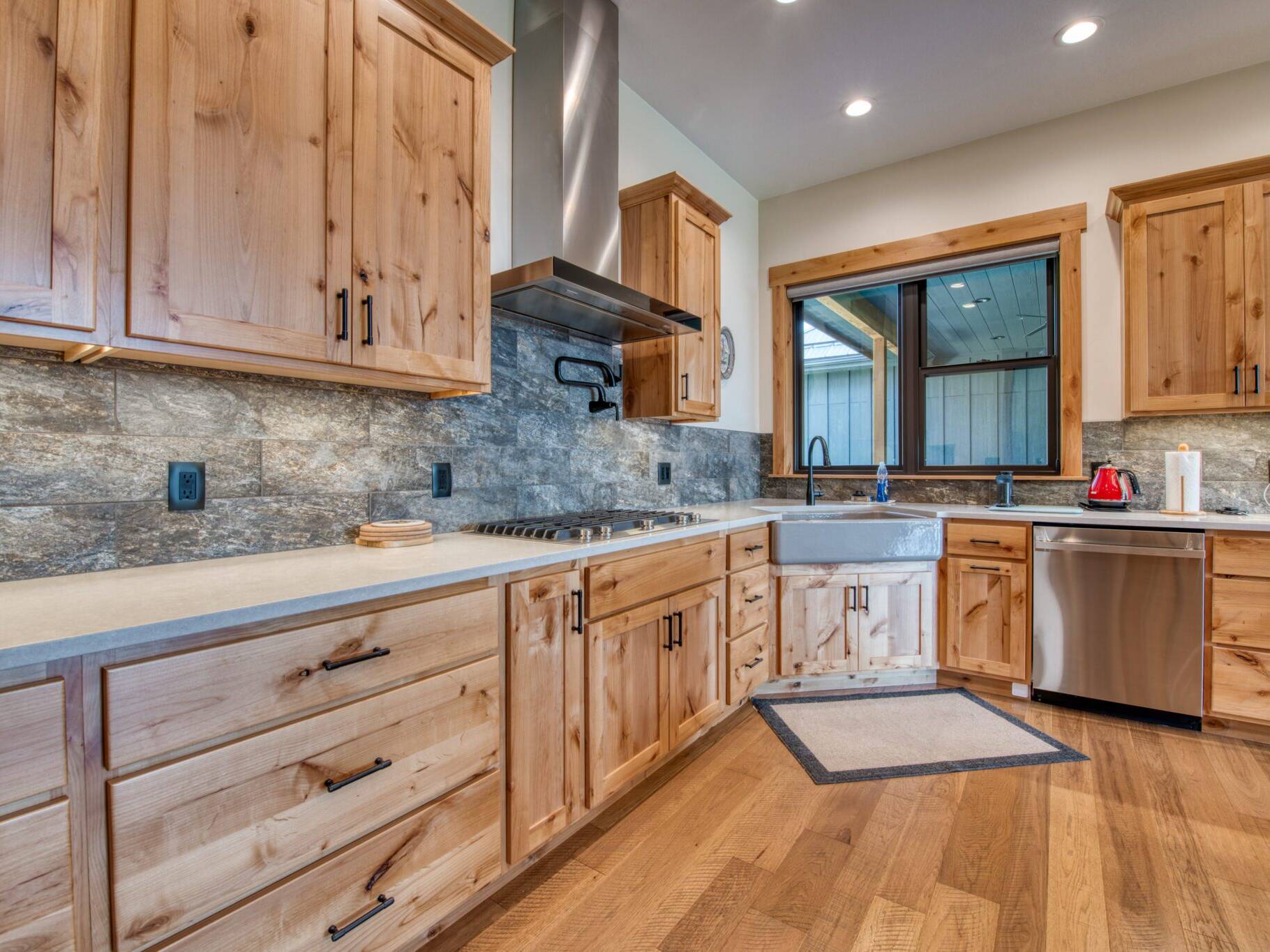 Kitchen with JenAir appliances, farmhouse sink, wood floors, alder cabinets, quarts countertops, and slate tile backsplash in a custom home built by Big Sky Builders of Monana in Florence, MT