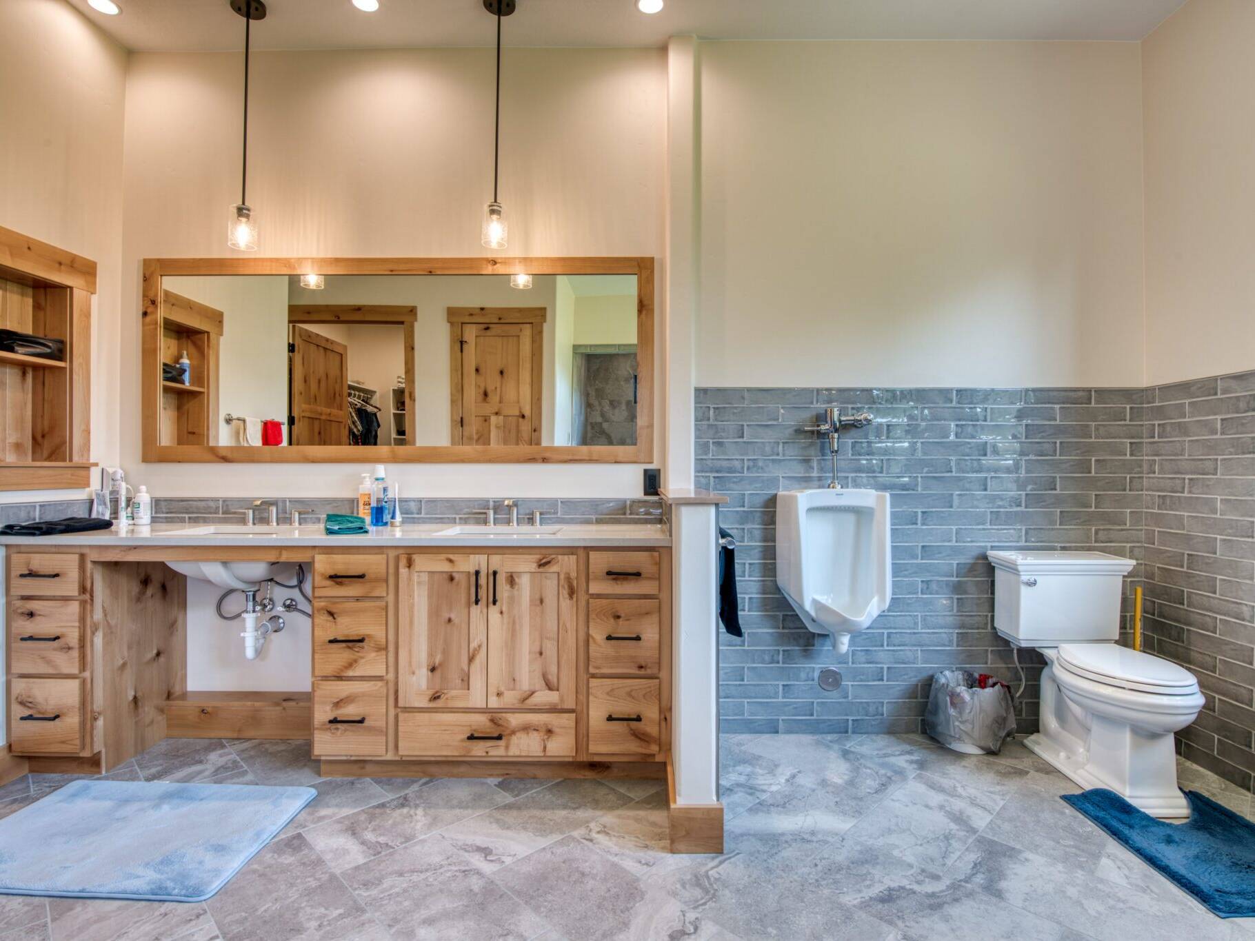 Master bathroom with rustic alder cabinets, quartz countertops, tile floor and wainscotting, and urinal in a custom home built by Big Sky Builders in Florence, MT