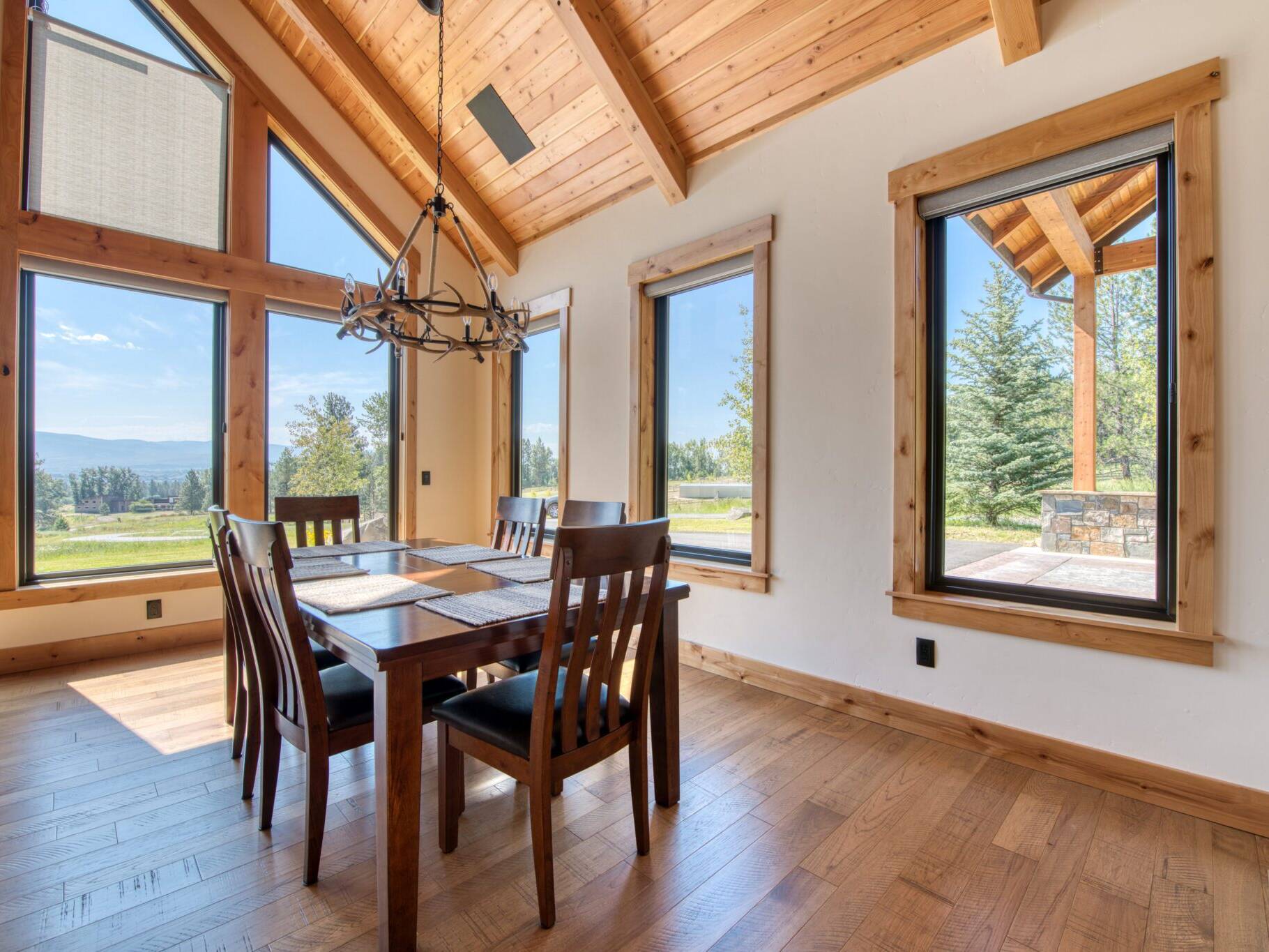 Dining room with wood floors, large windows, and a vaulted T&G ceiling with wood beam accents in a custom home built by Big Sky Builders of Montana in Florence, MT