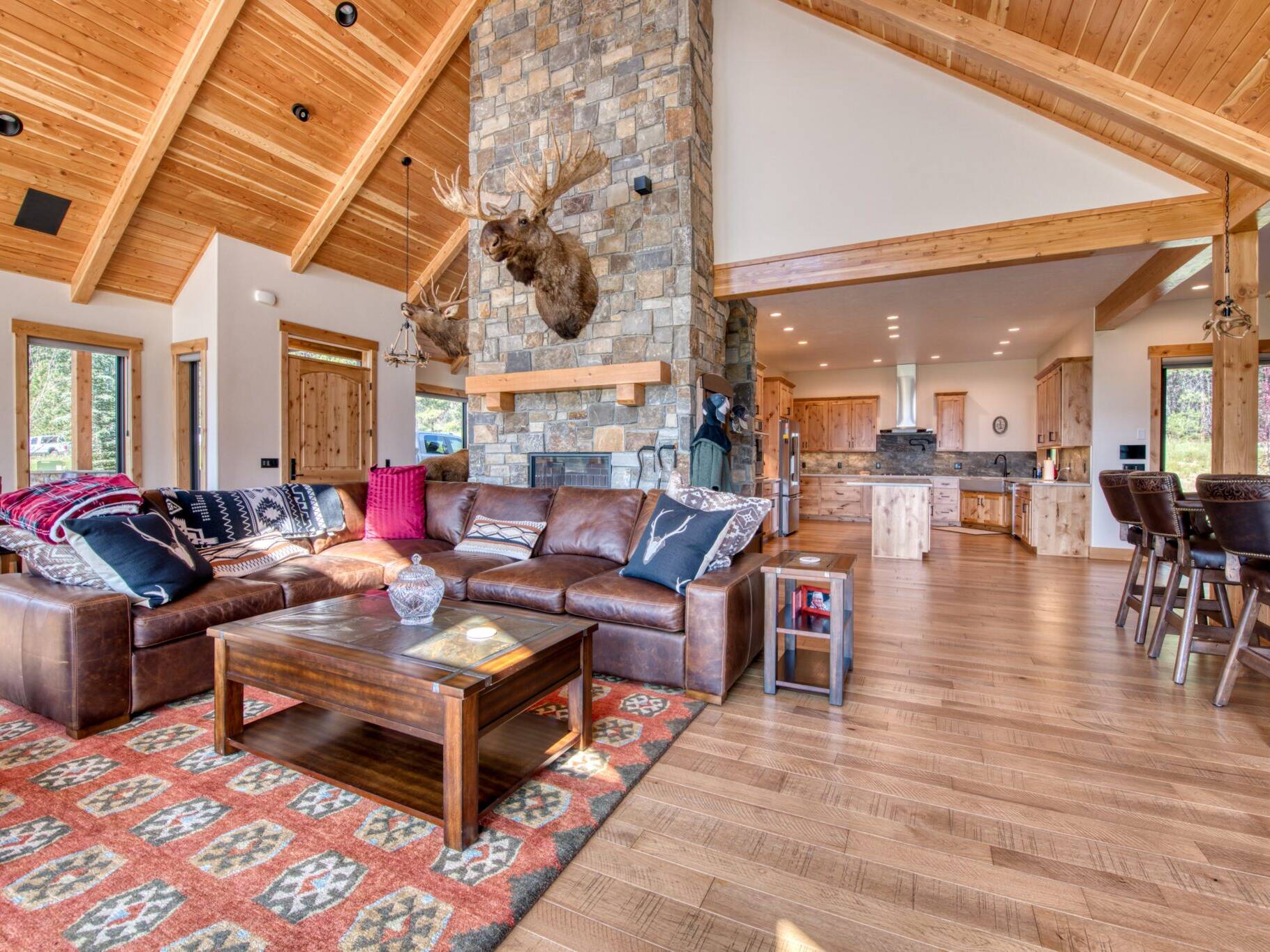 Great Room with wood floors, large windows, vaulted T&G ceiling with wood beam accents and large stone fireplace in a custom home built by Big Sky Builders of Montana in Florence, MT