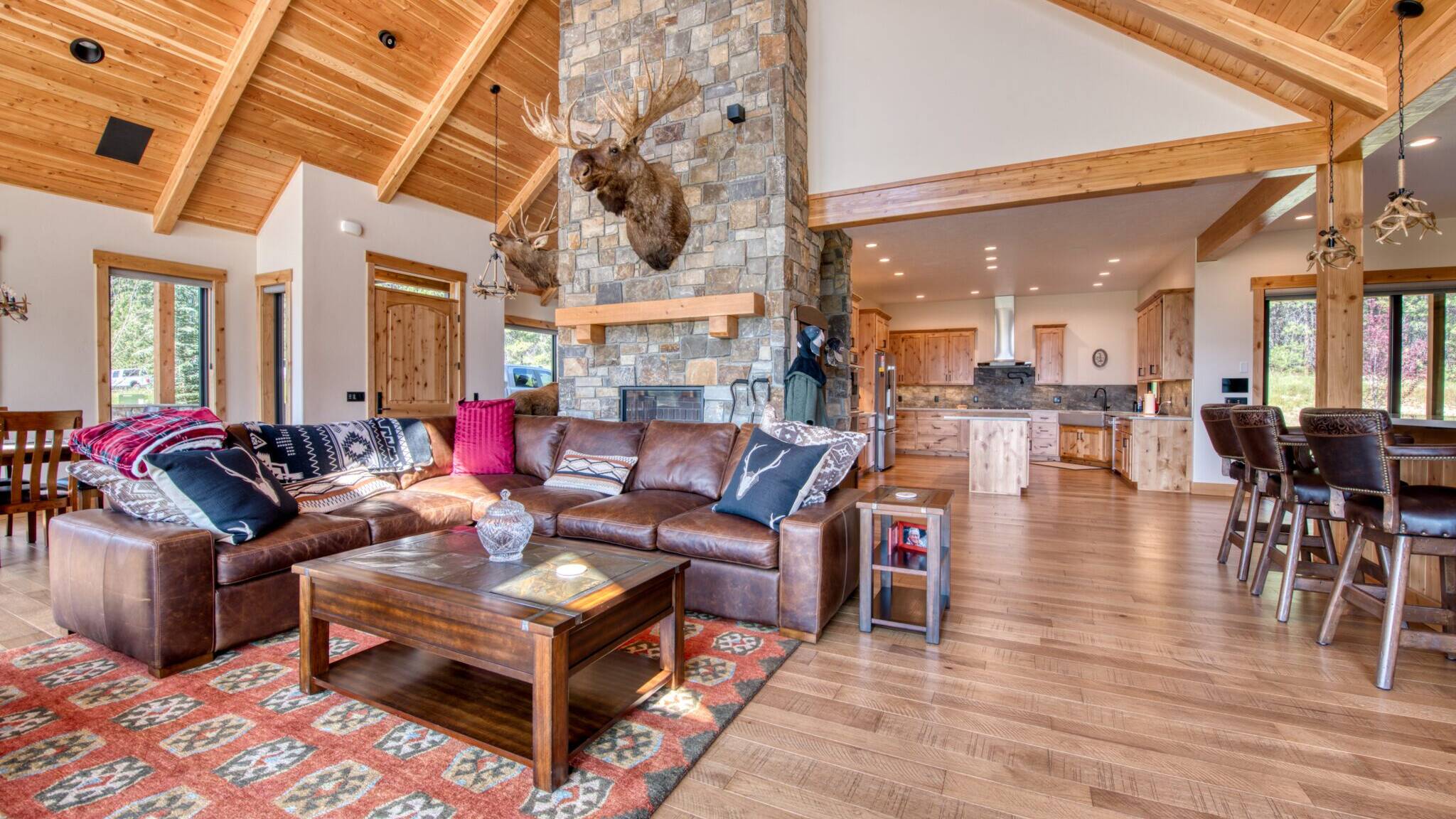 Great Room with wood floors, large windows, vaulted T&G ceiling with wood beam accents and large stone fireplace in a custom home built by Big Sky Builders of Montana in Florence, MT