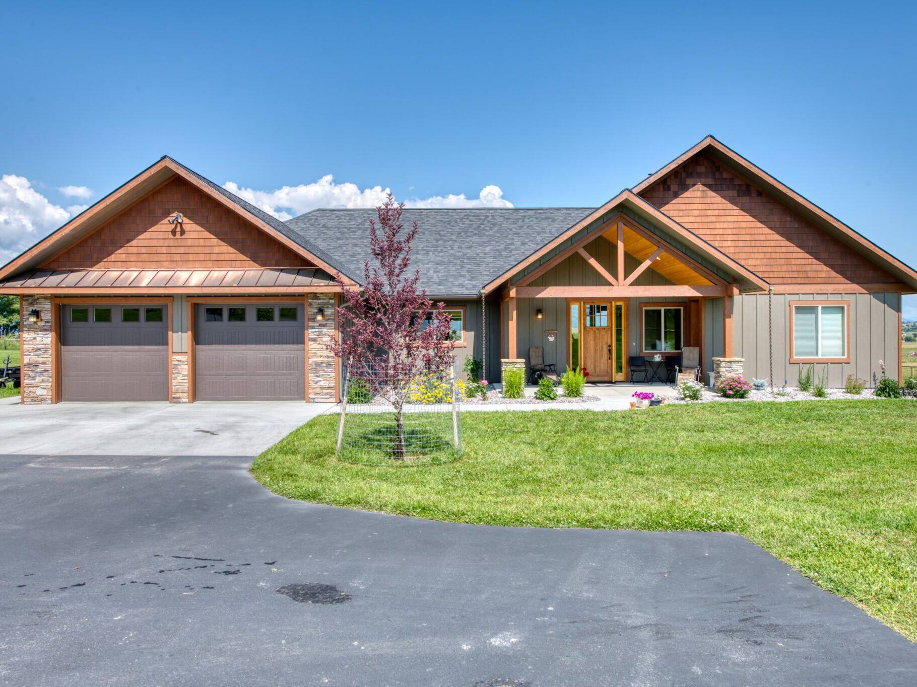 Front exterior, featuring a timber truss at the entry and a copper roof accent over the garage on a custom home built by Big Sky Builders in Stevensville, MT