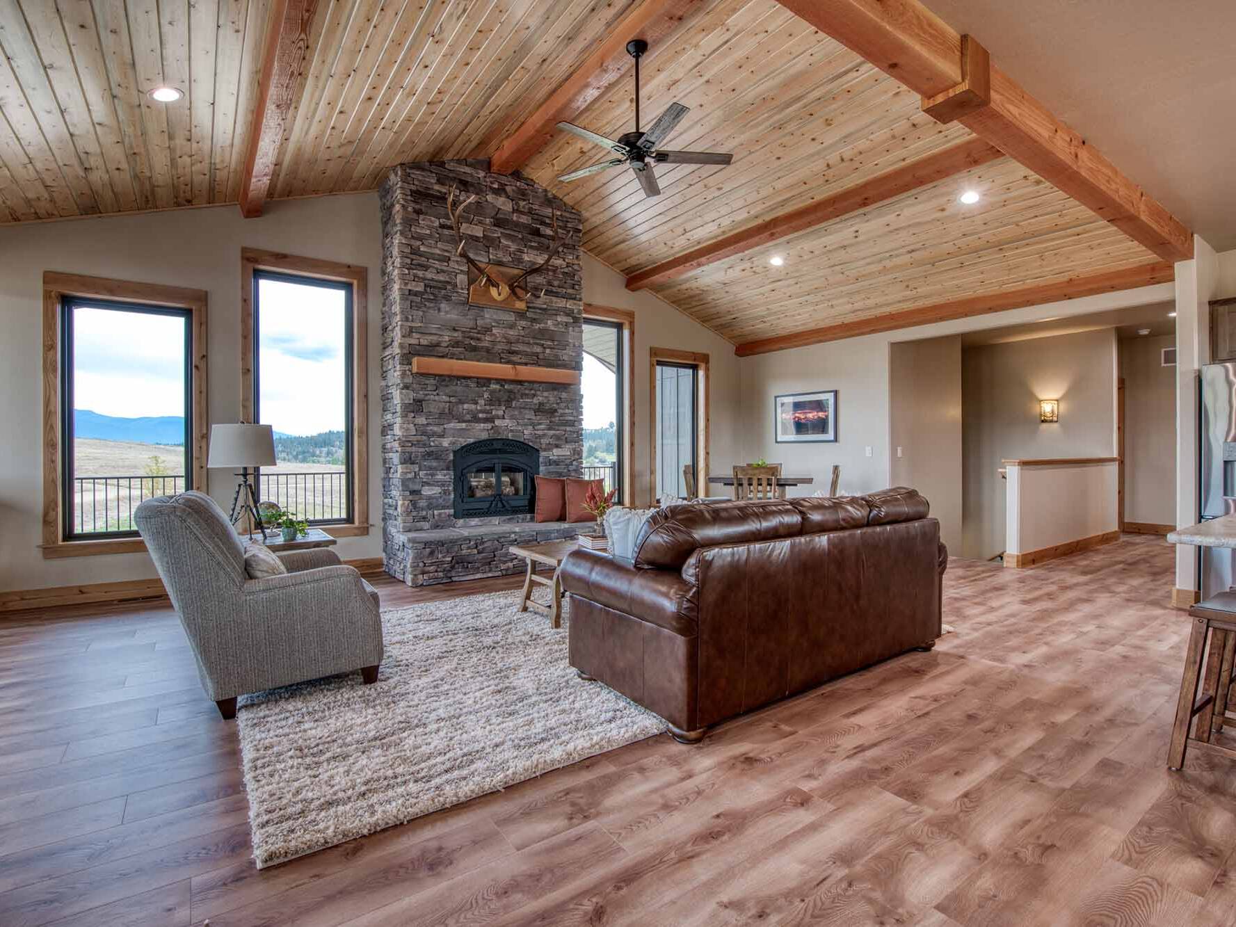 Living Room with a wood burning fireplace, vaulted ceiling, blue pine t&g ceiling, and timber accents in a custom home built by Big Sky Builders in Stevensville, MT