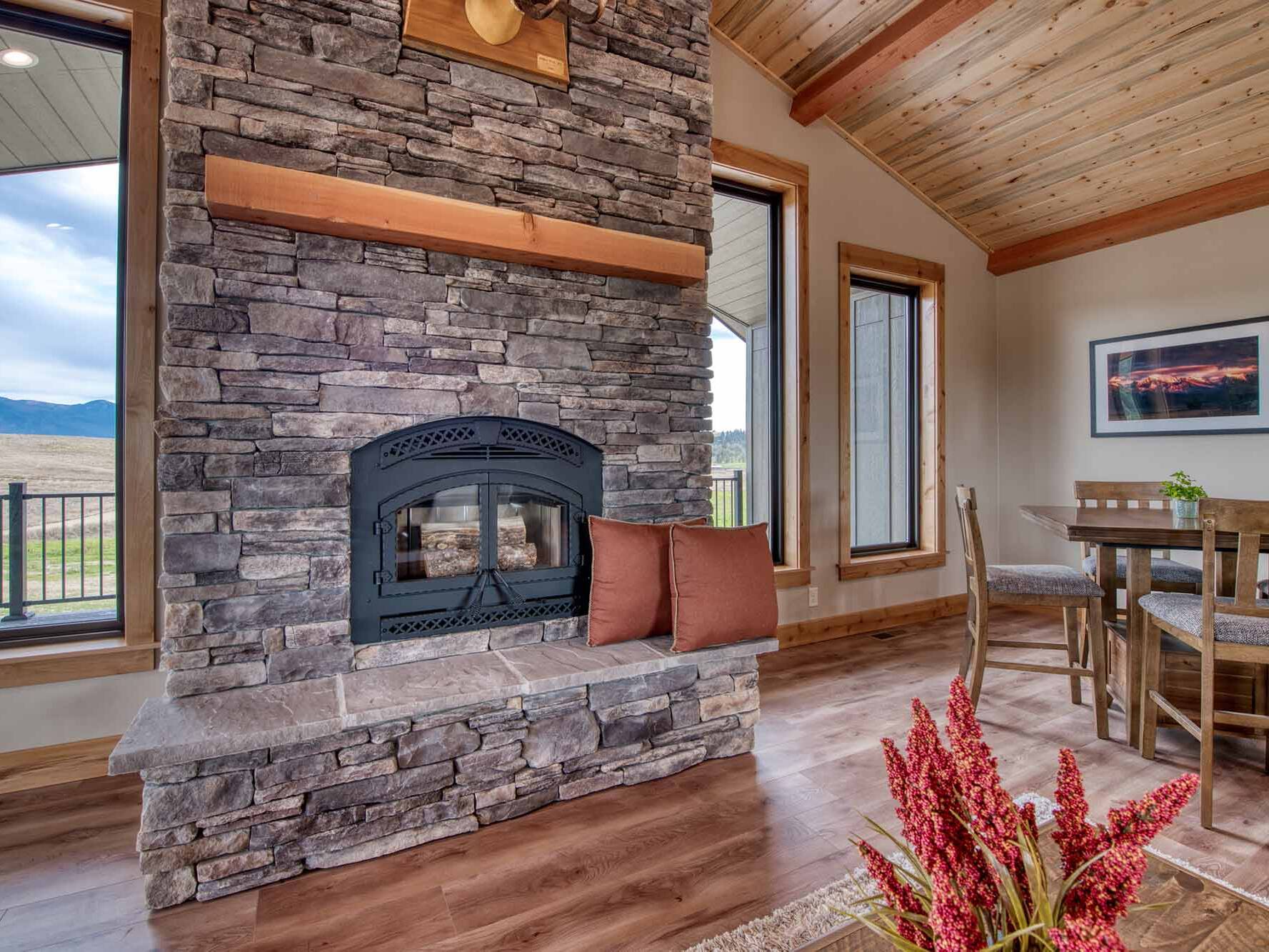 Living Room with a wood burning fireplace, vaulted ceiling, blue pine t&g ceiling, and timber accents in a custom home built by Big Sky Builders in Stevensville, MT