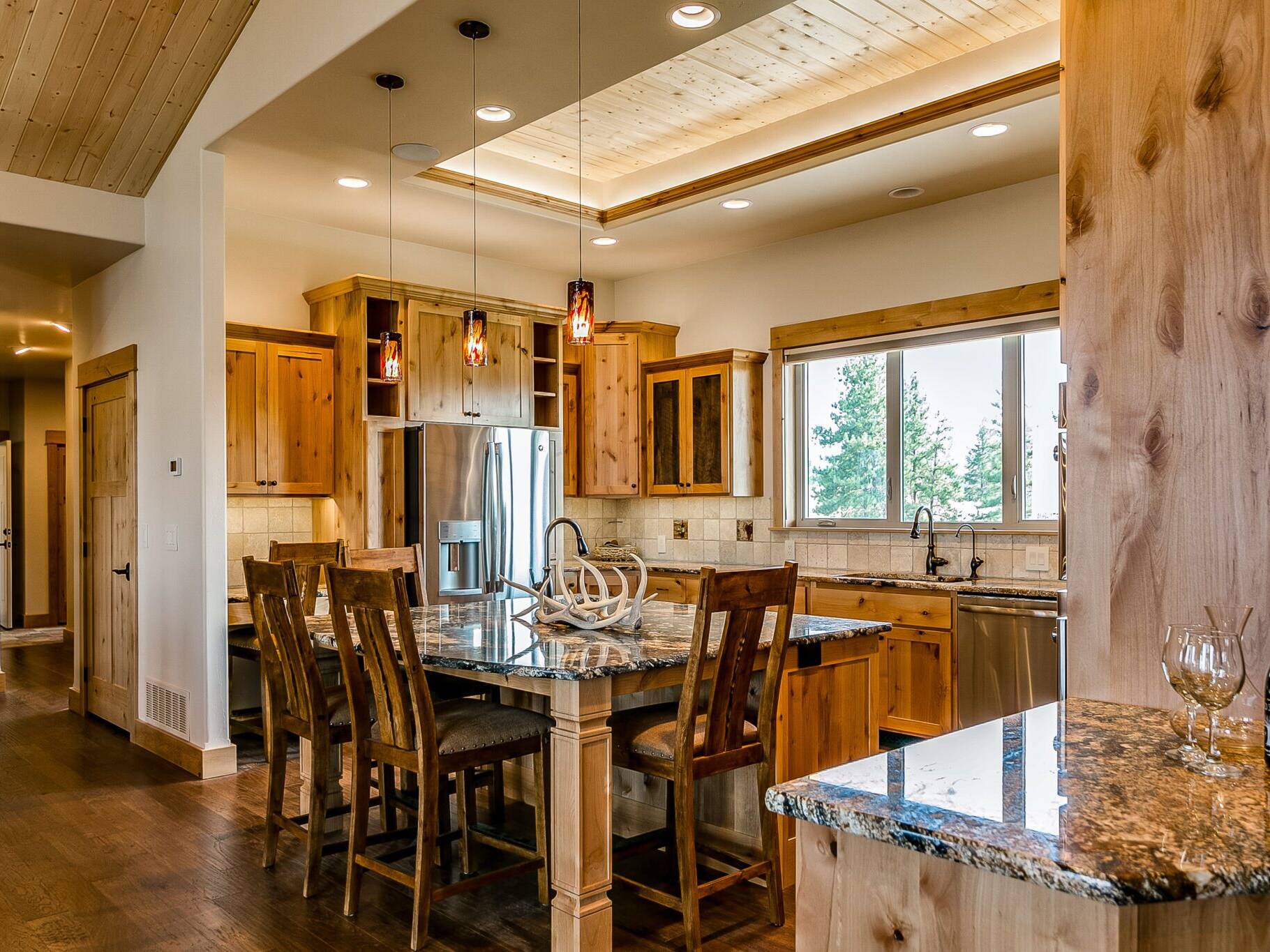 Kitchen with tray ceiling with T&G pine, rustic alder cabinets, granite countertops, and wood floor in a custom home built by Big Sky Builders near Stevensville, Montana
